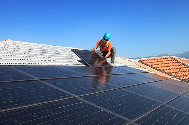 Professional contractor installing black solar panels on a residential roof under a clear blue sky.