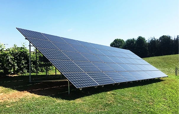 A large ground-mounted solar panel array installed on a grassy field for renewable energy.