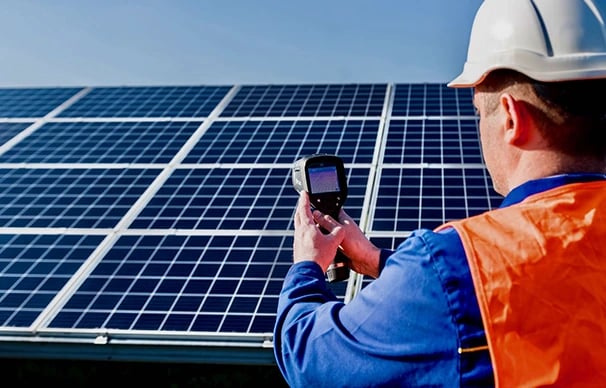 A technician performing a thermal inspection of solar panels using a handheld infrared camera.