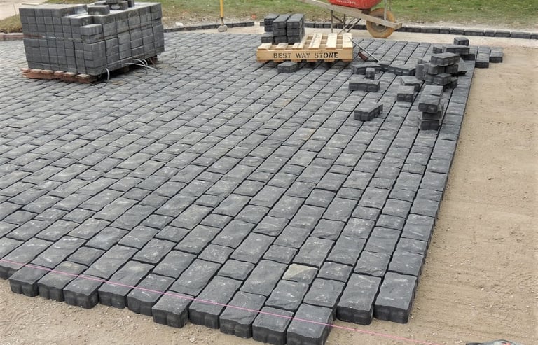 Professional installation of a charcoal grey cobblestone paver driveway on a prepared sand base.