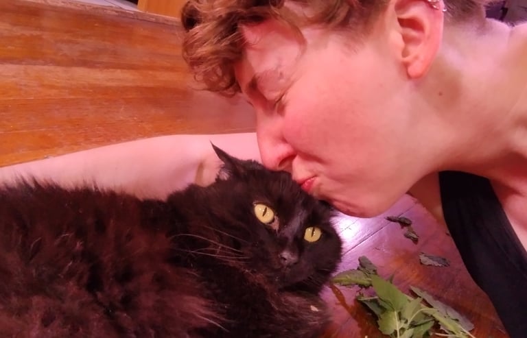 Cassie is lying on the floor kissing their sister's black cat with catnip on the floor