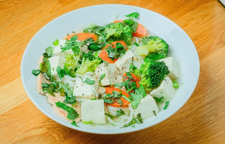 Bowl of Vietnamese noodle soup with sliced beef, bean sprouts, herbs, and lime on a wooden table