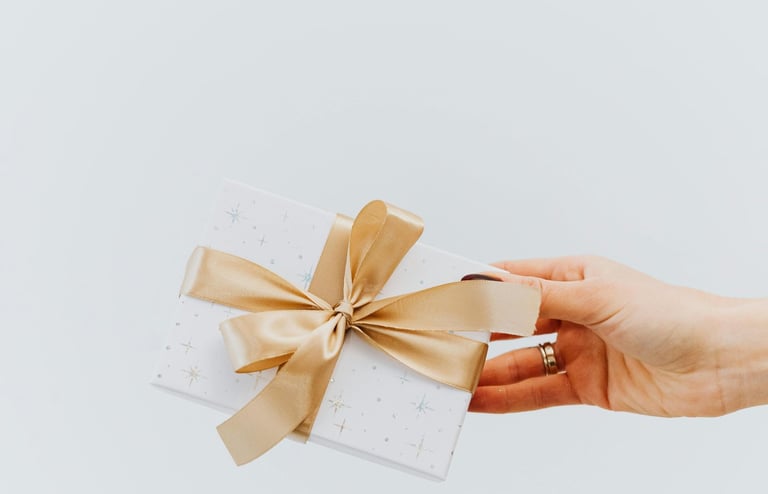 Woman's hand holding a gift card wrapped in white paper and with a gold bow