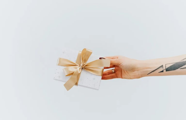 Hand with tattoo holding a white patterned gift card with a gold satin bow.