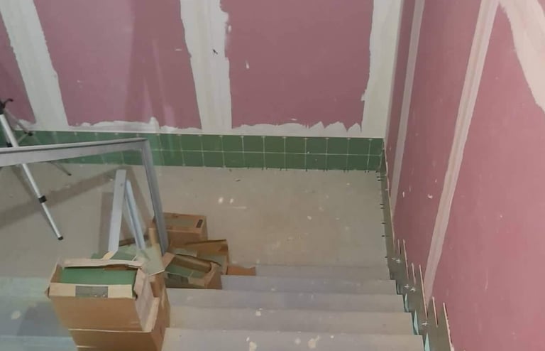 Concrete stairs under renovation with pink drywall and green ceramic tile backsplash installation.