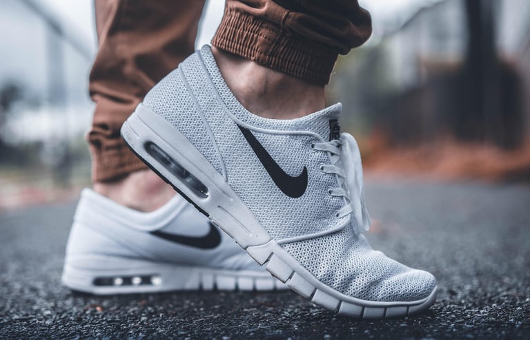 Close-up of a person wearing light gray Nike sneakers with mesh fabric on an urban street.