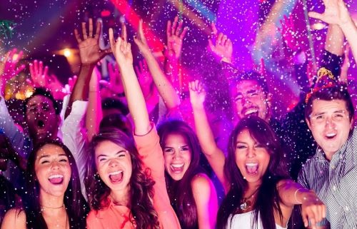 Excited crowd of friends cheering at a nightclub party with falling confetti and colorful lights.