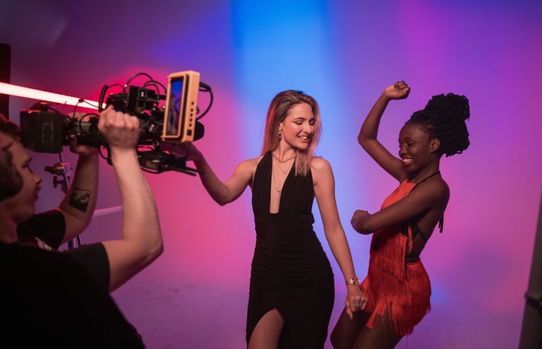 Two women stand in front of a studio camera dancing 