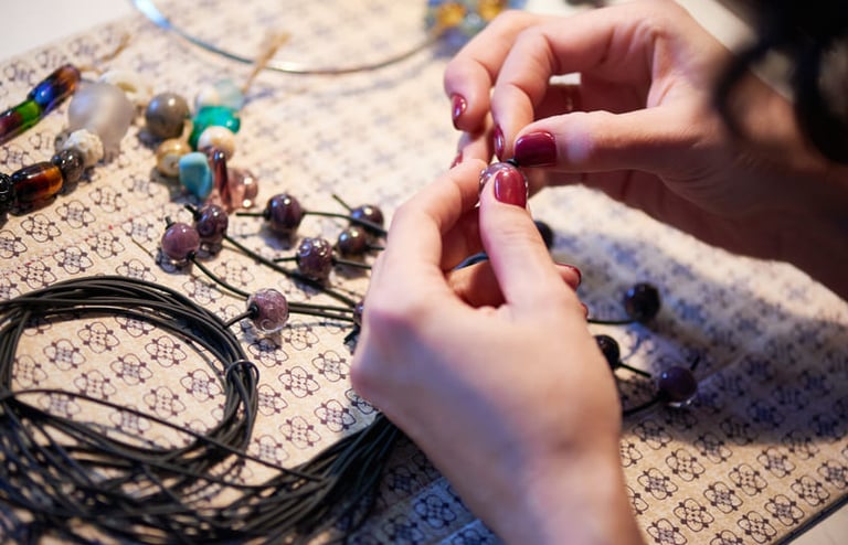 Manos artesanas ensartando cuentas de vidrio hechas a mano en un cordón para un collar de joyería.