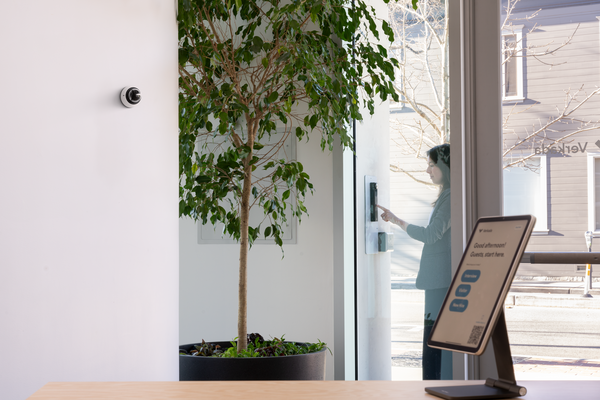 Visitor using Verkada intercom system at secure building entrance, monitored by indoor surveillance camera