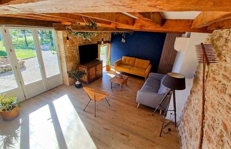 Grand salon de 30 m² avec murs en pierre, poutres apparentes, canapés confortables et télévision