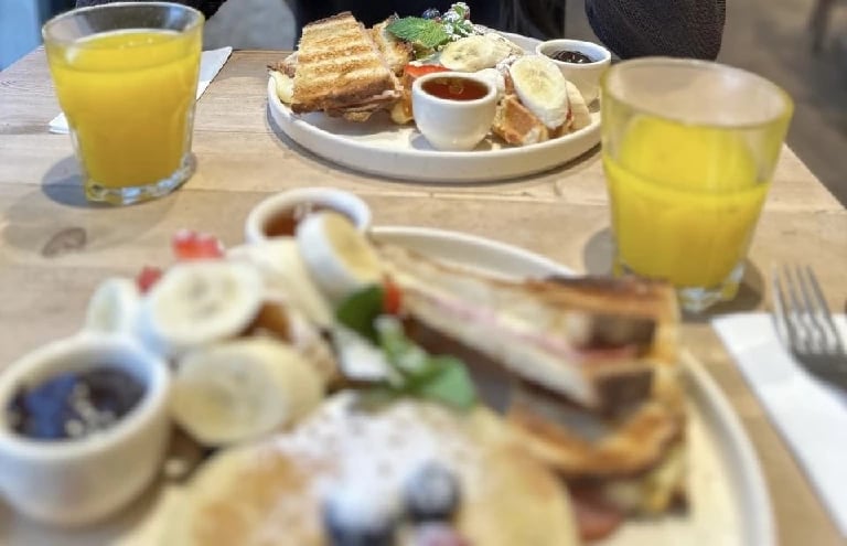 Assiettes de brunch avec pancakes, fruits, gaufres, confitures et verres de jus d’orange.