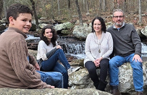 a family sitting on a rock formation in a wooded area