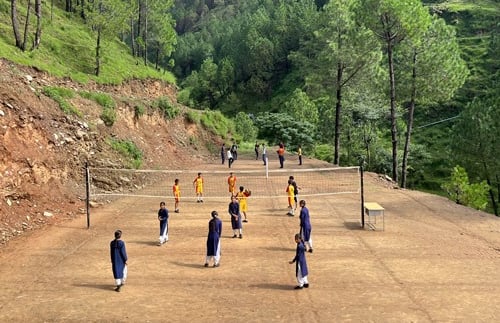 Section of bare earth carved out of mountain. Girls playing volleyball.side with