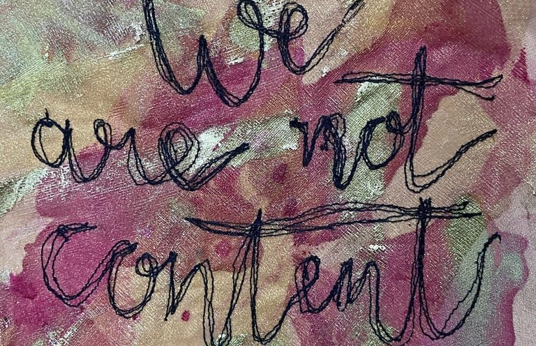 machine embroidered text which says 'we are not content' in cursive writing on a pink background