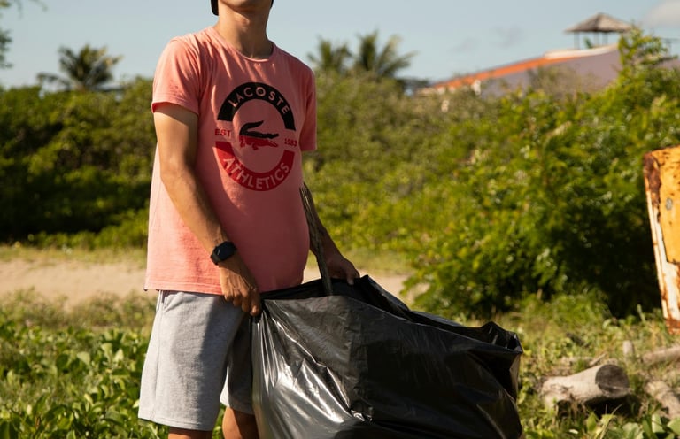 A young volunteer holding a large black trash bag during a community beach cleanup project.