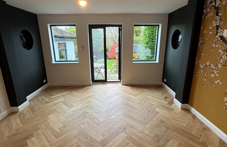 Modern living room with herringbone oak wood flooring, black accent walls, and floral mural in Hove.