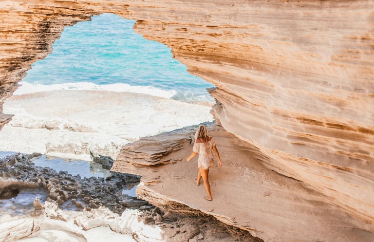 Woman walking along coastal cliff edge overlooking sandy beach and Ocean