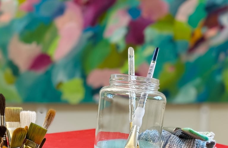 Painting tools and brushes on studio worktable with colorful painting in background