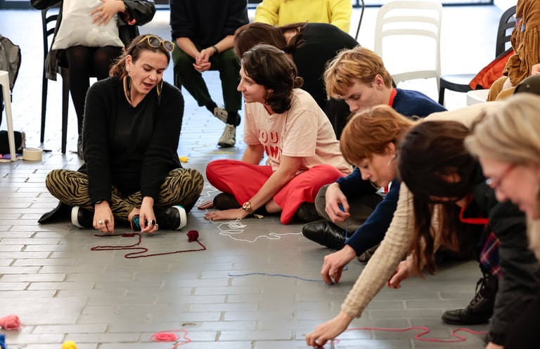 A group of people sitting on the floor drawing their journeys using yarn.