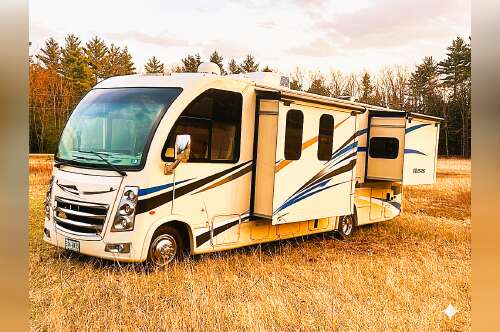 A white Class A motorhome RV parked in a field with slides extended for luxury camping.