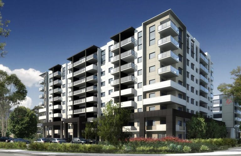 Nine-story apartment building in white and beige, featuring landscaped sidewalks with plants.