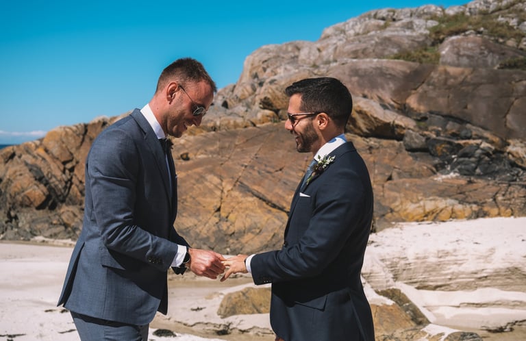 a man in a suit and tie on a beach exchanging rings