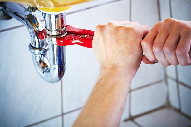 man using a red mini pipe wrench to turn a pipe under the sink