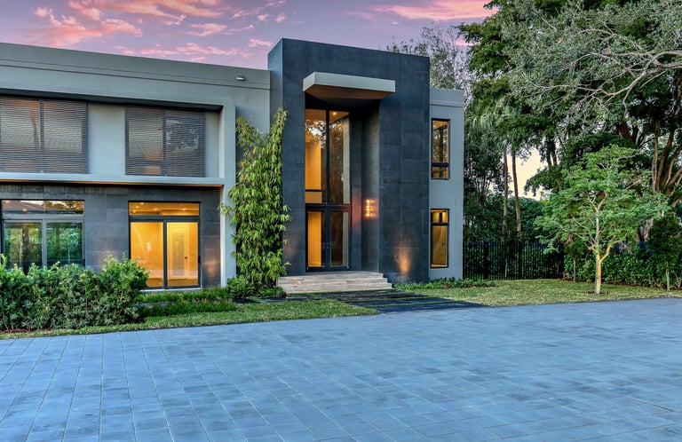 a luxury home lit up at night with a large driveway and a vibrantly colored sky