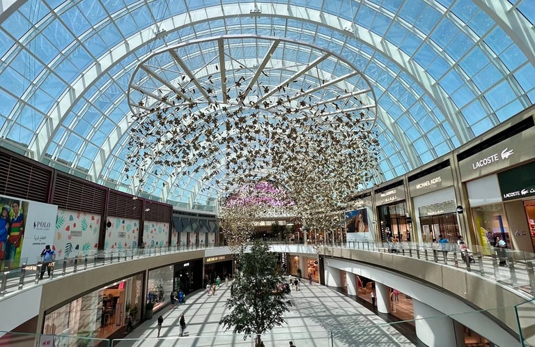 a large atrium with a tree in the middle inside Dubai Hills Mall