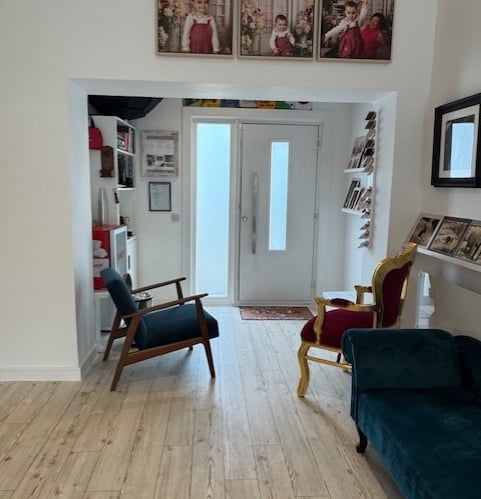 Modern studio entryway featuring light oak flooring, velvet armchairs, and framed family portraits.