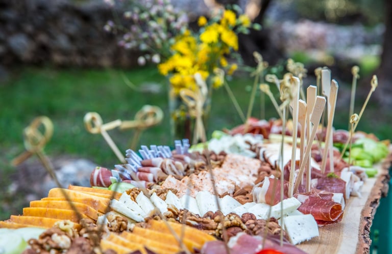 Rustic wood slab charcuterie board with gourmet cheeses, cured meats, and nuts at an outdoor picnic.