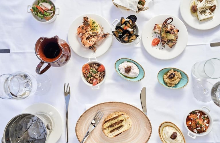 An overhead view of a Mediterranean seafood spread with grilled octopus, mussels, and shrimp on a white tablecloth.
