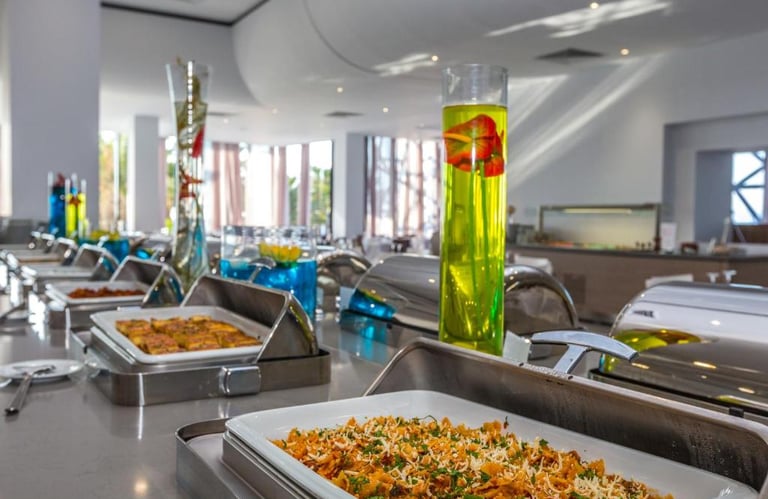 Gourmet hotel buffet with hot pasta dishes in silver chafing servers and tall decorative vases.
