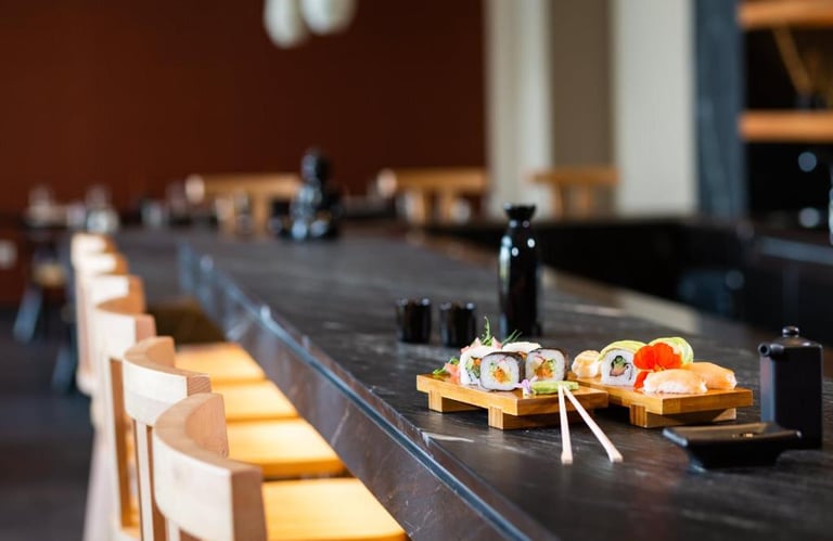 Fresh sushi rolls and nigiri served on wooden platters at a modern dark stone restaurant bar.