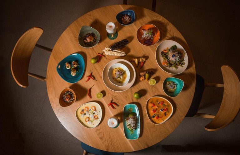 Overhead view of a round wooden table featuring various colorful Peruvian ceviche dishes and tapas.