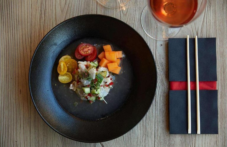 Fresh white fish ceviche served with cherry tomatoes and melon in a black bowl with rose wine.