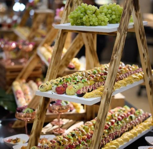 Elegant tiered wooden ladder display featuring assorted gourmet sushi rolls and fresh green grapes at a buffet.