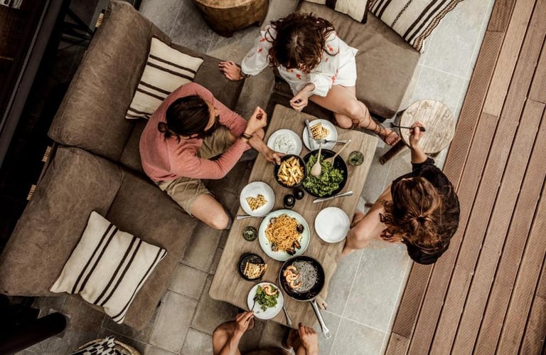 Aerial view of friends sharing a Mediterranean dinner on a modern outdoor patio lounge.