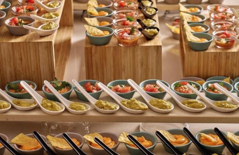 Gourmet catering appetizers featuring individual servings of guacamole, salsa, and cheese dip on bamboo platters.