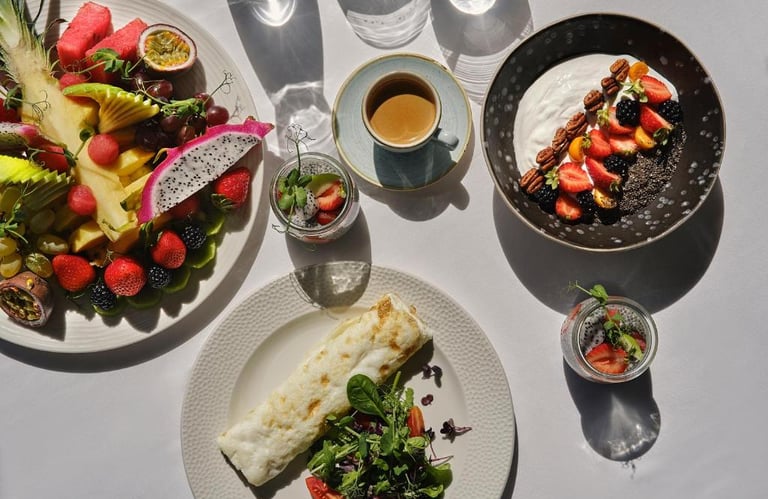 Healthy breakfast spread with fruit platter, yogurt bowl, egg wrap, and coffee in morning sunlight.