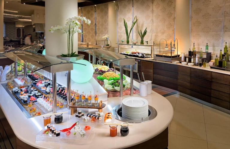 Luxury hotel buffet featuring a fresh sushi display, salad bar, and gourmet appetizers in a modern dining room.