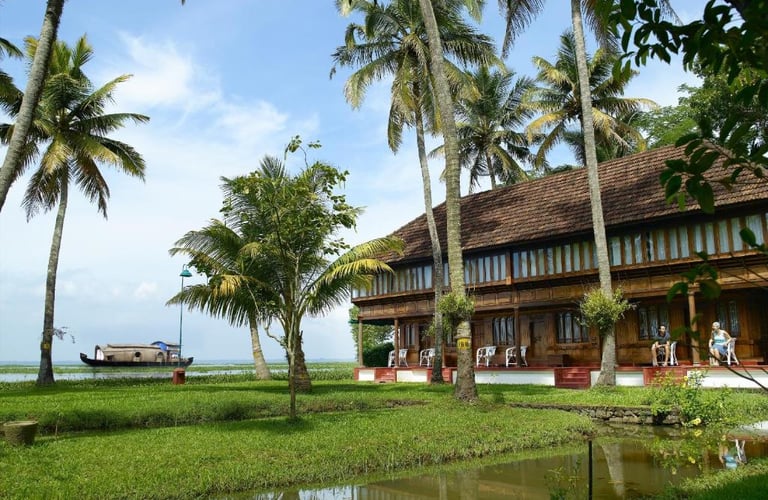 Traditional Kerala house surrounded by palm trees and lush greenery, overlooking tranquil backwaters.