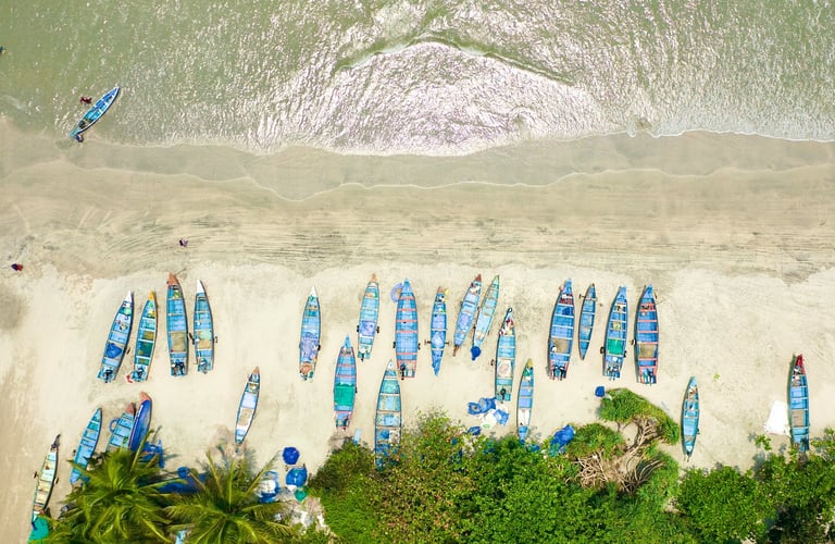 Aerial view of colorful fishing boats lined along the sandy shore of Kerala's drive-in beach, surrounded by lush greenery