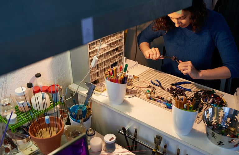 Joyera usando pinzas en una mesa de trabajo, con cuentas y herramientas para la creación de joyería.