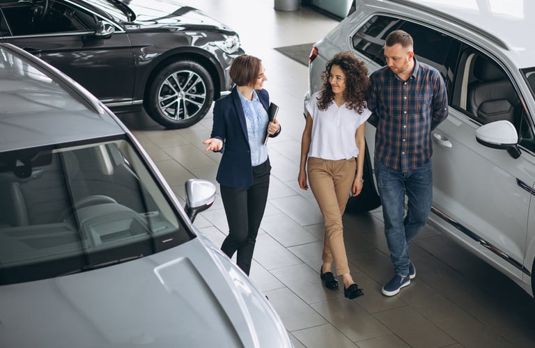  A female car saleswoman talks to a couple, walking through a car showroom.