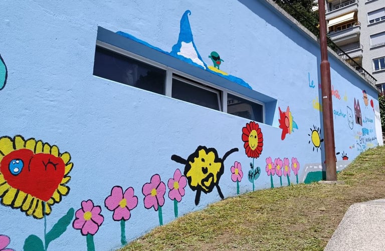 Murales colorato realizzato con bambini, fiori e sole su parete azzurra, progetto artistico colletti
