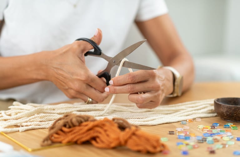 Manos sobre una mesa cortando un hilo para realizar un bordado en macramé