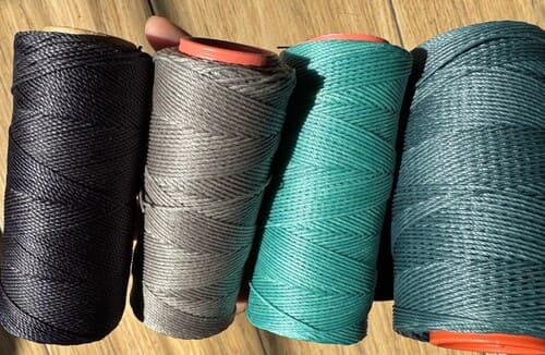 Cuatro bobinas de hilo de poliéster encerado de alta calidad en negro, gris, verde azulado y verde.