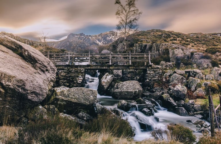 Rustic wooden bridge over a cascading waterfall in the rocky Snowdonia mountain landscape.